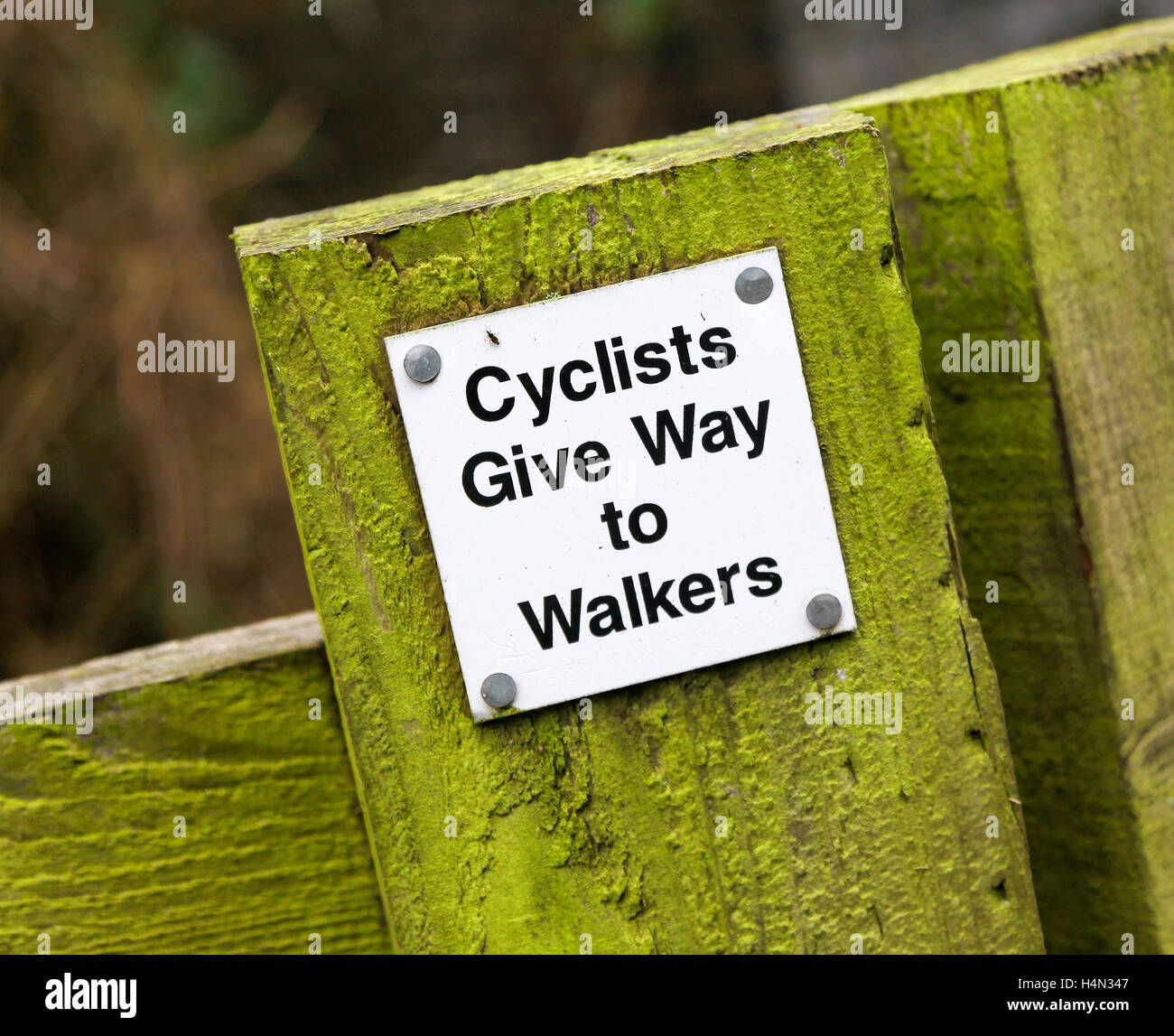 Un segno che dice ciclisti dare il posto ai camminatori su una posta di legno, Inghilterra, Regno Unito Foto Stock