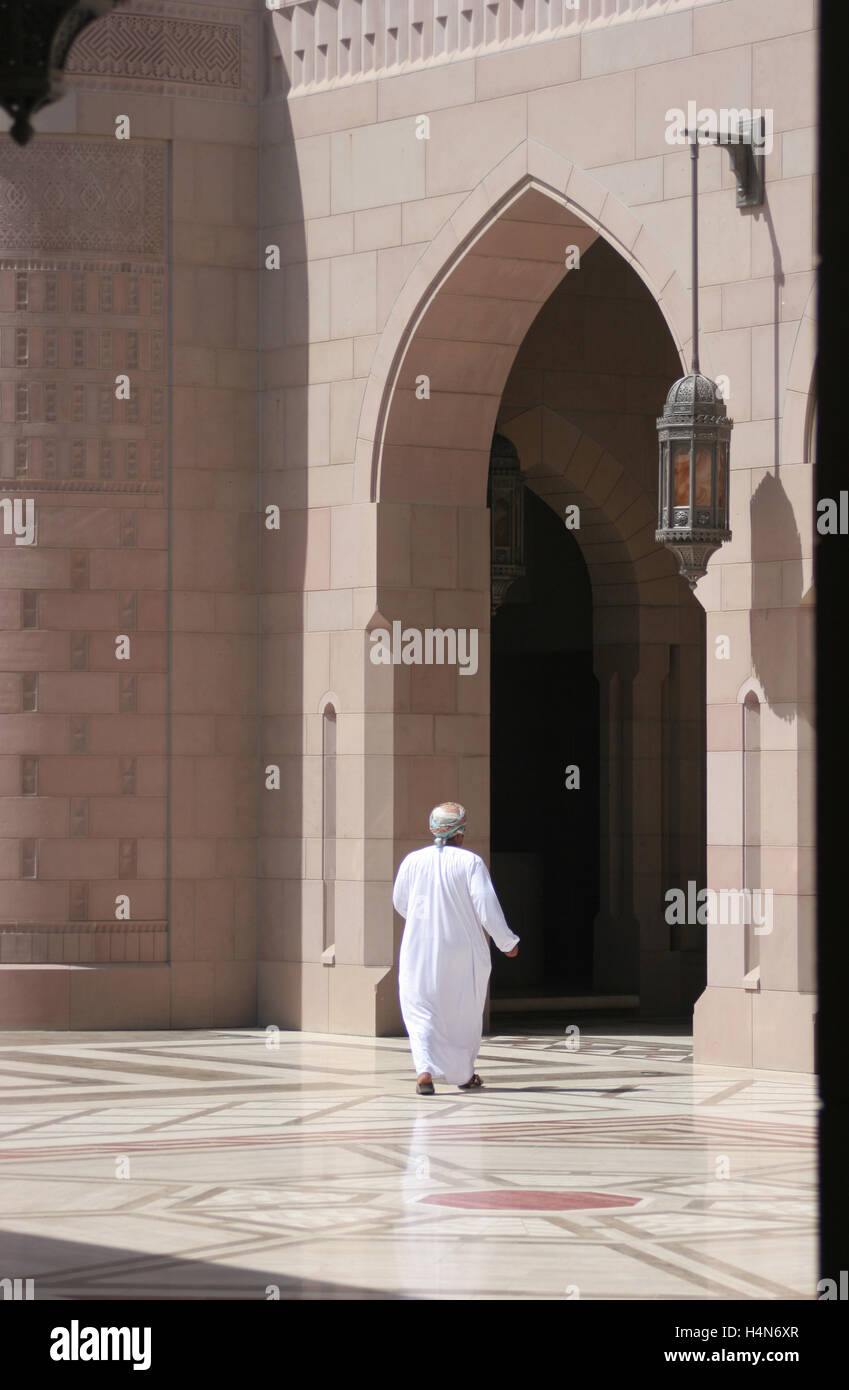 Un adoratore in tradizionali abiti arabi cammina verso un grande arco presso la grande moschea in Muscat Oman Foto Stock