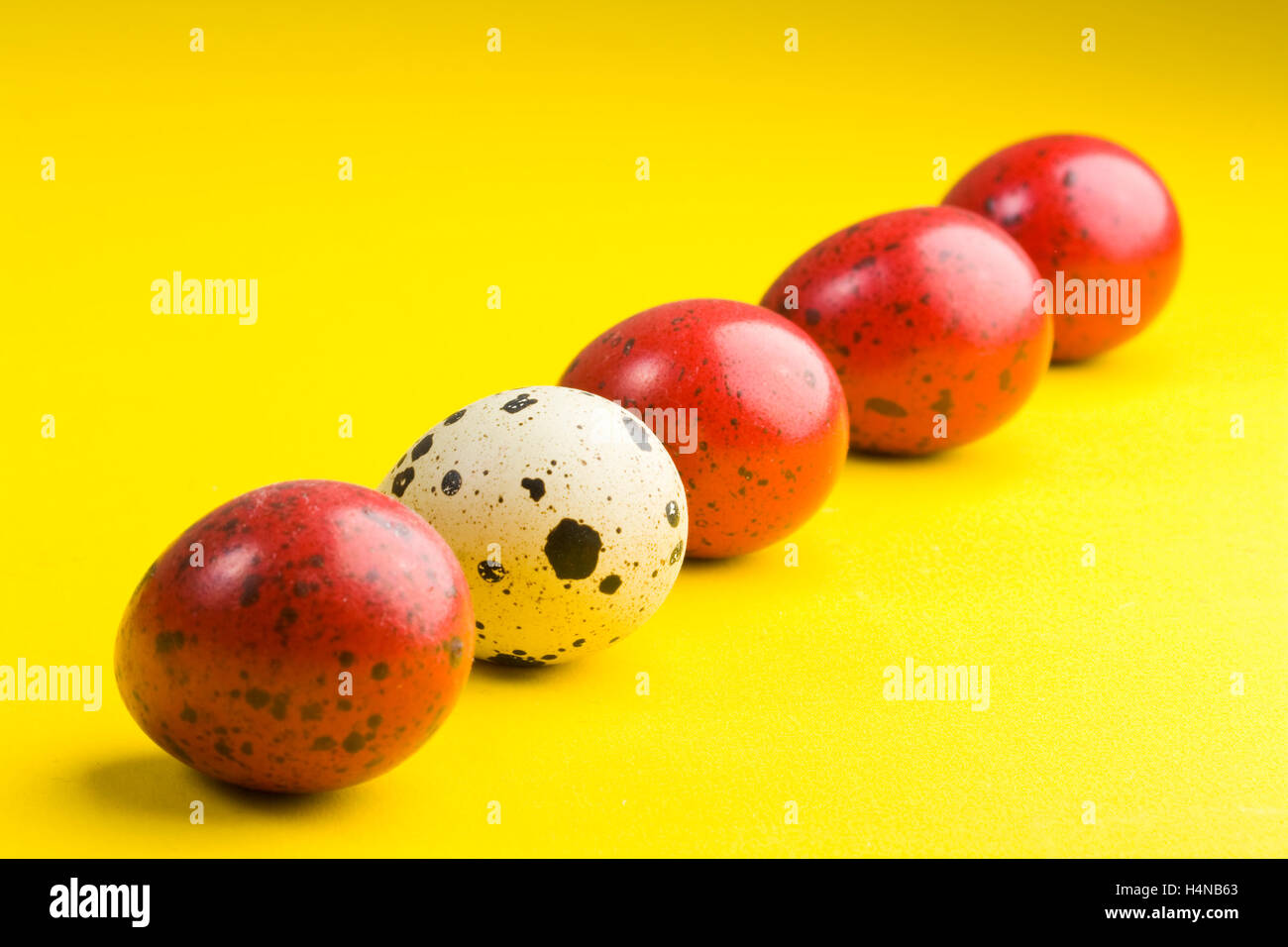 Uova colorate con una diversa su sfondo giallo con ombra Foto Stock