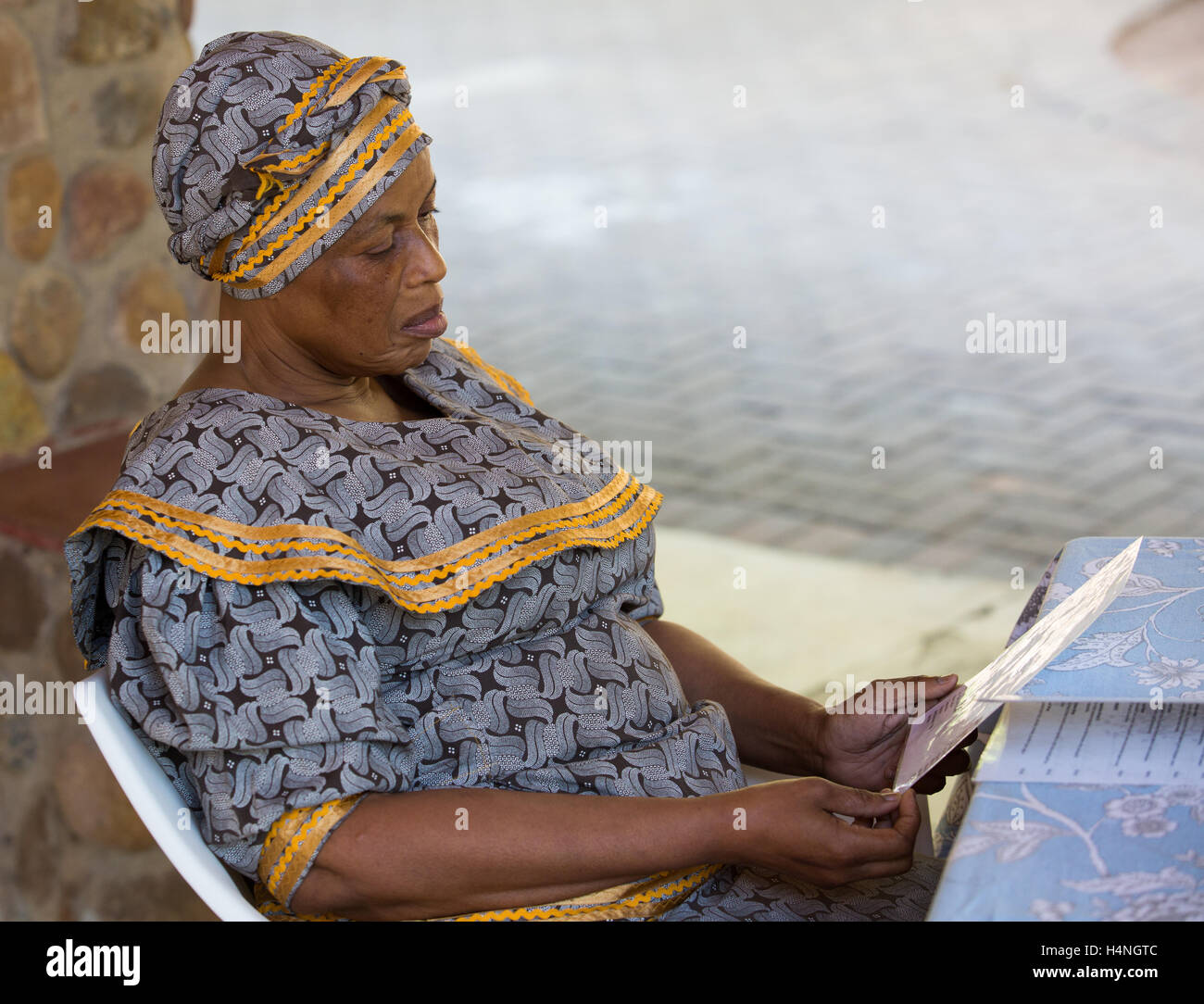 Ritratto di una donna africana nel tradizionale abito seshweshwe lettura del menu in un ristorante all'aperto Foto Stock