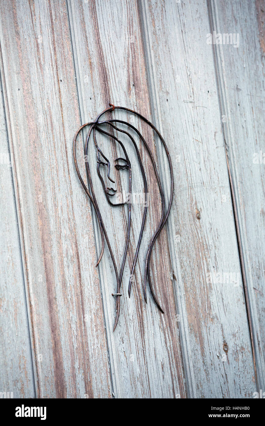 Un filo metallico di scultura di un volto di donna su un asse di legno parete. Foto Stock