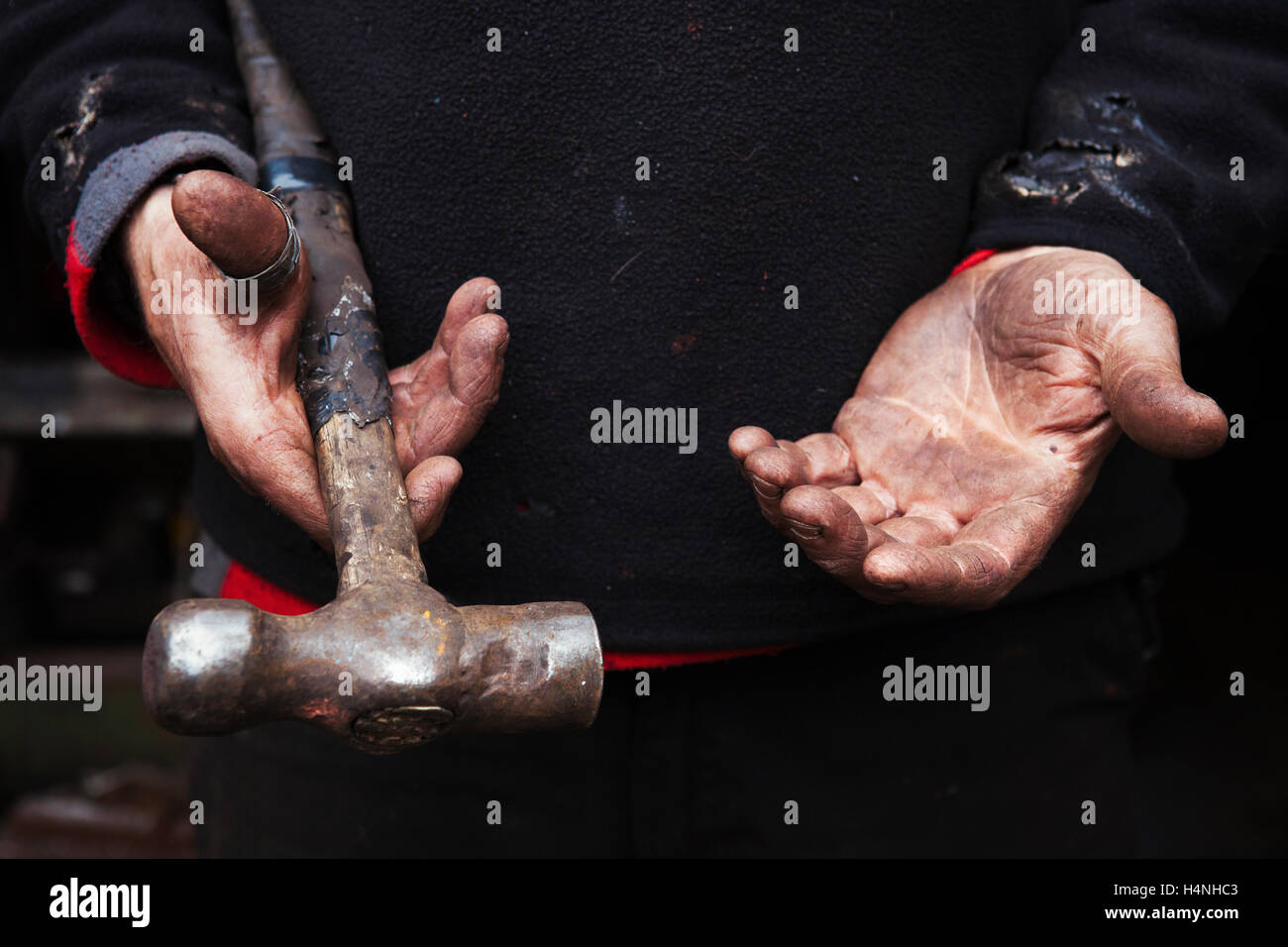 Close up di un fabbro con le mani in mano, tenendo in mano un martello metallico. Foto Stock