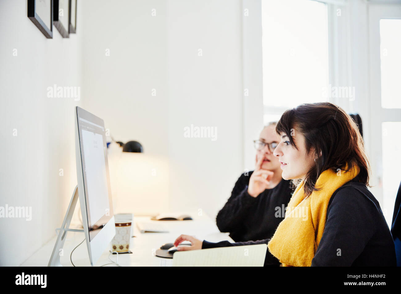 Due donne seduti condividere lo schermo di un computer e di discutere il contenuto grafico. Foto Stock