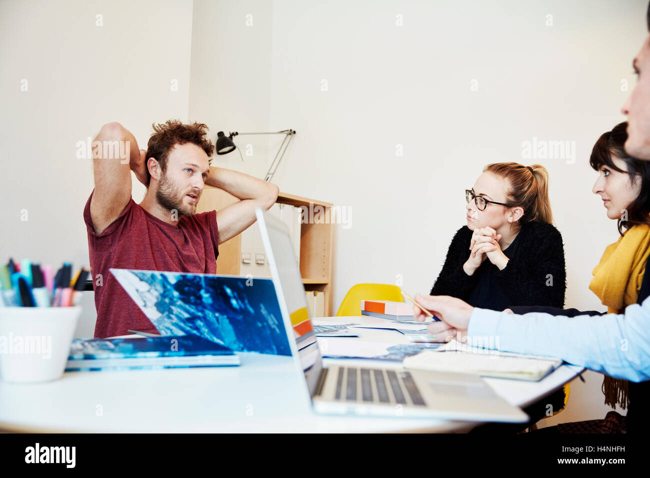 Quattro persone in occasione di una riunione, due uomini e due donne. Un computer portatile, carta e note i libri sul tavolo. Foto Stock