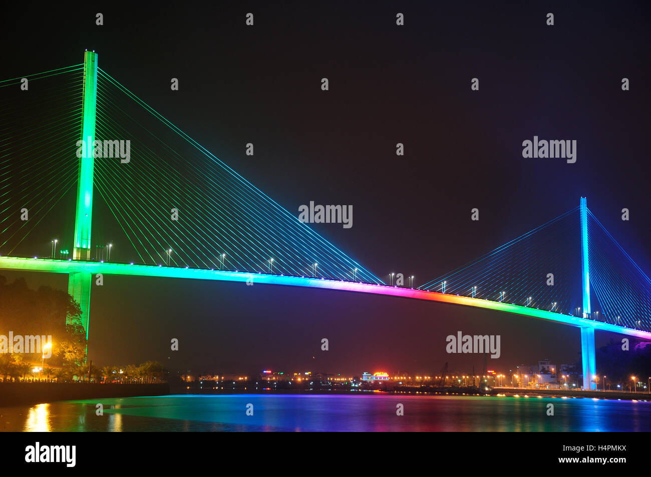 Il Bai Chay Bridge in HaLong Vietnam illuminato con rainbow illuminazione colorata di notte riflettendo nella Baia di Ha Long. Foto Stock