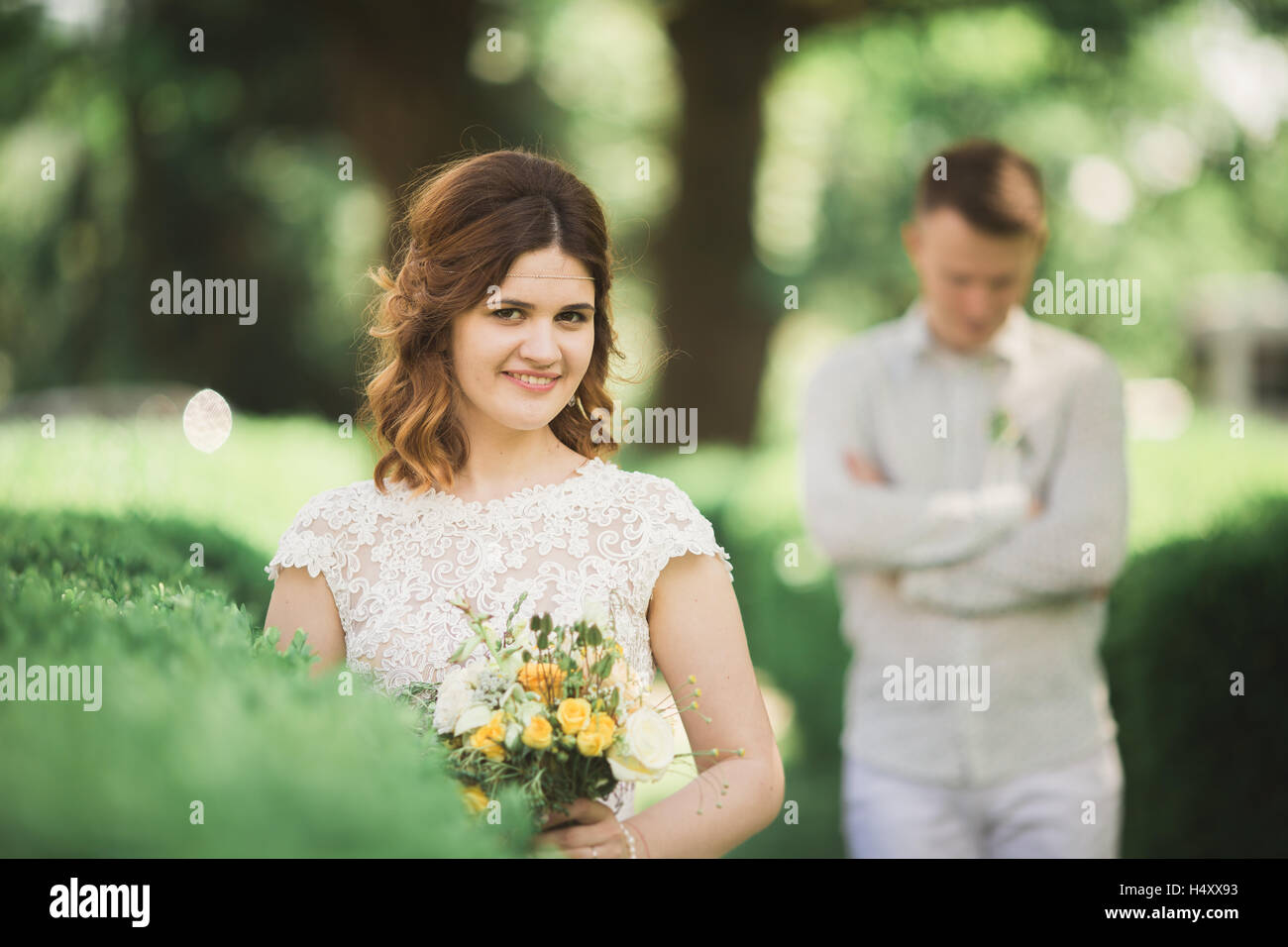 Sposa in posa e sorrisi mentre lo sposo attende sullo sfondo Foto Stock