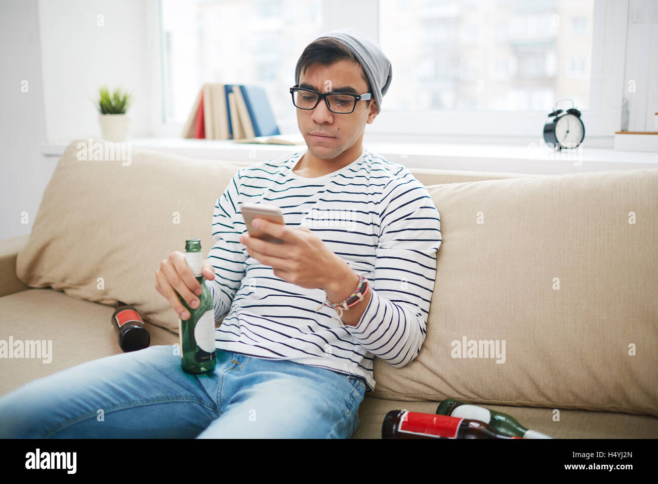 Guy moderno con la bottiglia vuota e telefono cellulare sms di scrittura a casa Foto Stock