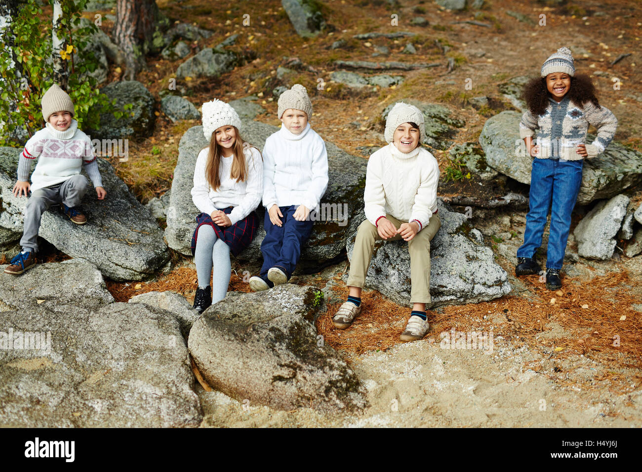 Carino kids in elegante-casual wear seduto su pietre in ambiente naturale Foto Stock