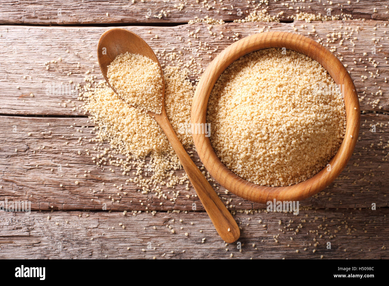 Couscous crudo in una ciotola di legno e il cucchiaio sul tavolo. Orizzontale vista superiore Foto Stock