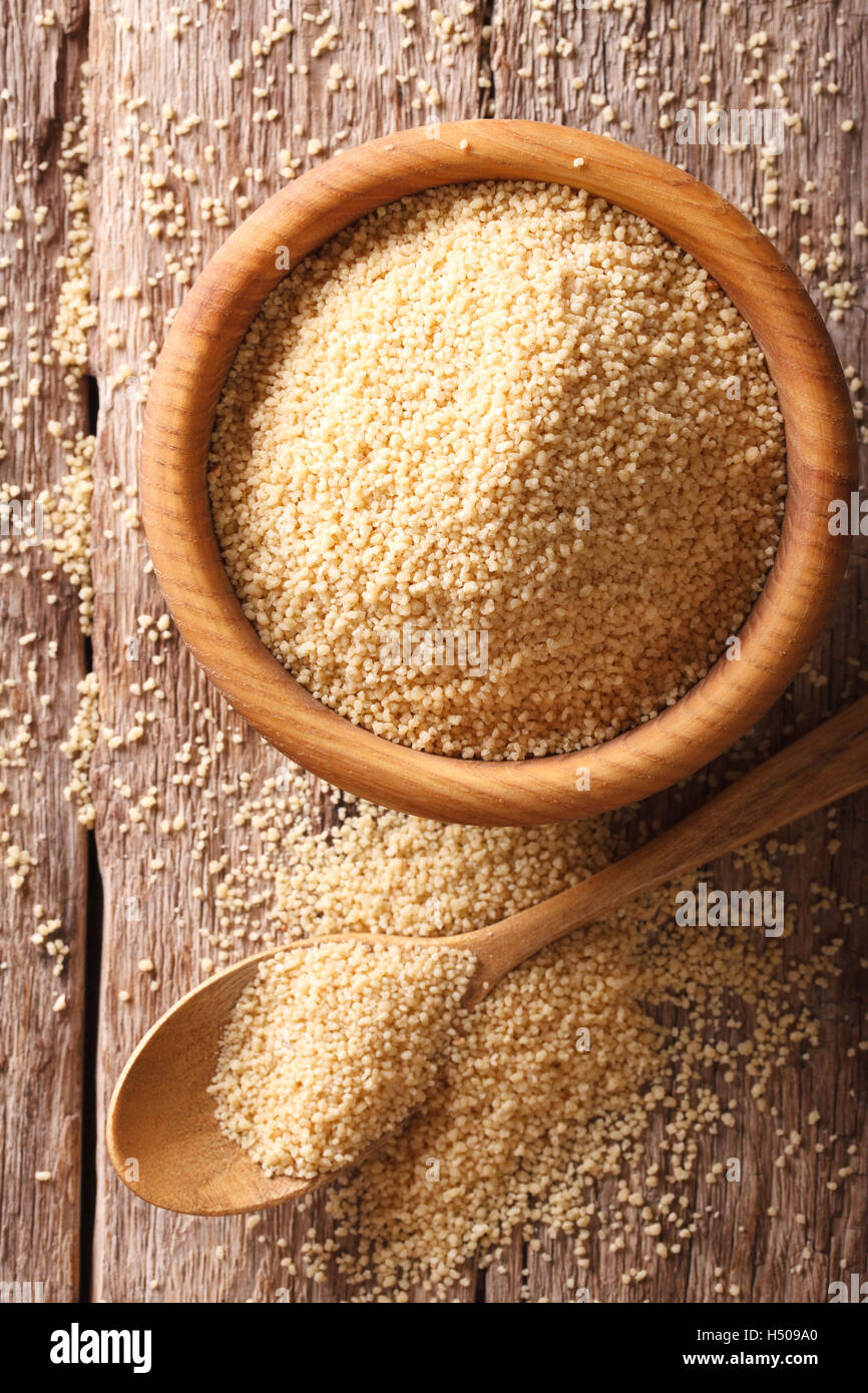 Couscous crudo in una ciotola di legno e il cucchiaio sul tavolo di close-up. verticale vista superiore Foto Stock