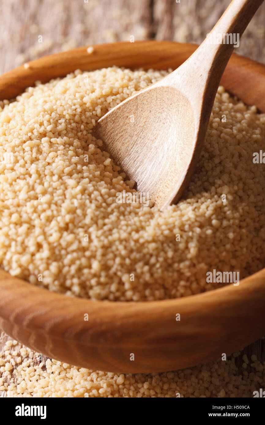 Il cous cous a secco in una ciotola di legno con un cucchiaio macro sul tavolo. In verticale Foto Stock