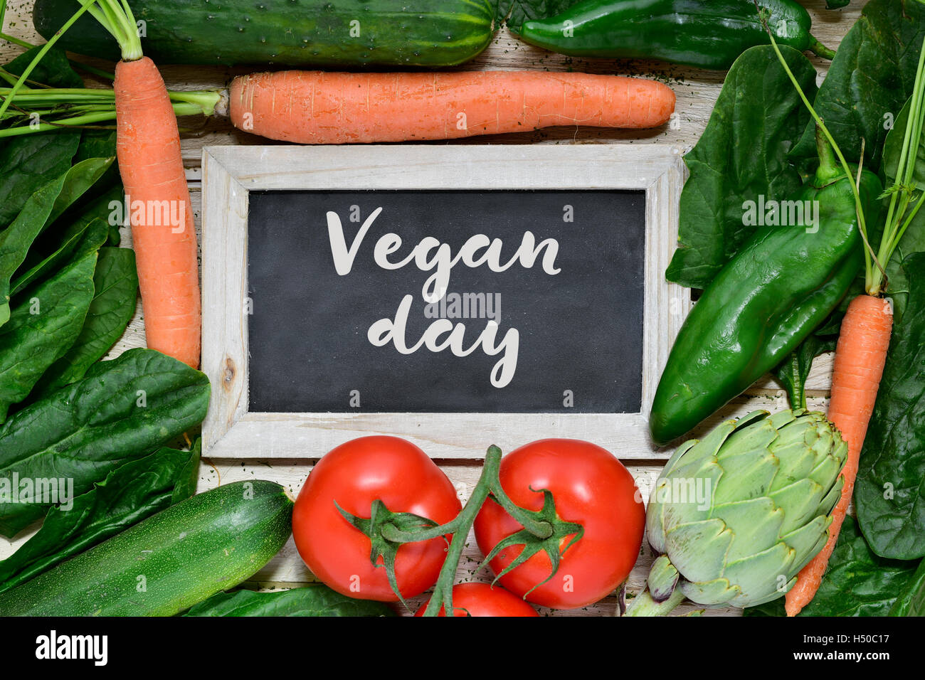 Alta angolazione di una superficie di legno pieno di diverse verdure crude e una lavagna con il testo vegan giorno scritto in esso Foto Stock