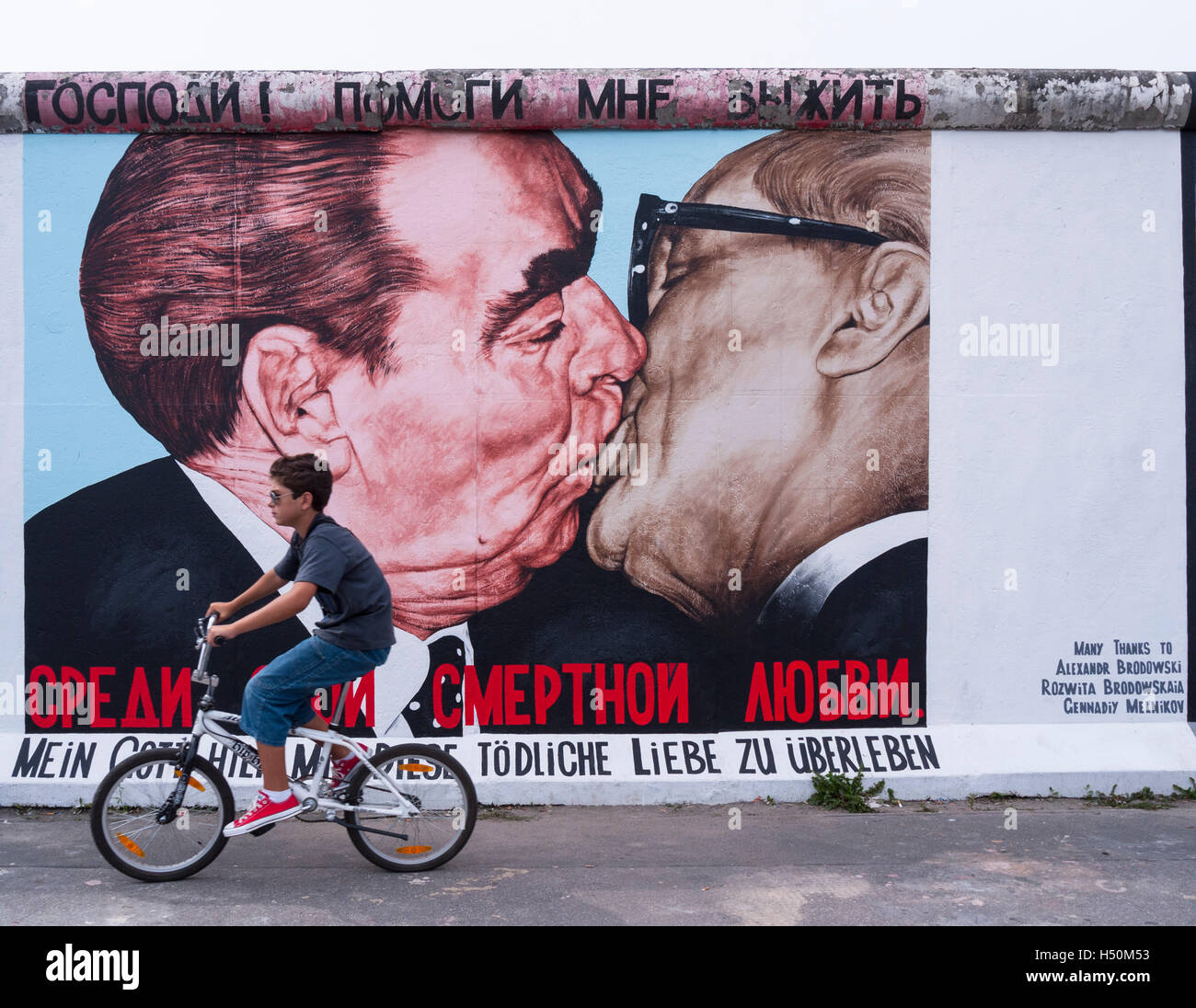 Cicli di ragazzo passato murale di Brezhnev kissing Honecker a East Side Gallery a muro di Berlino in / Friedrichshain Kreuzberg di Berlino Foto Stock