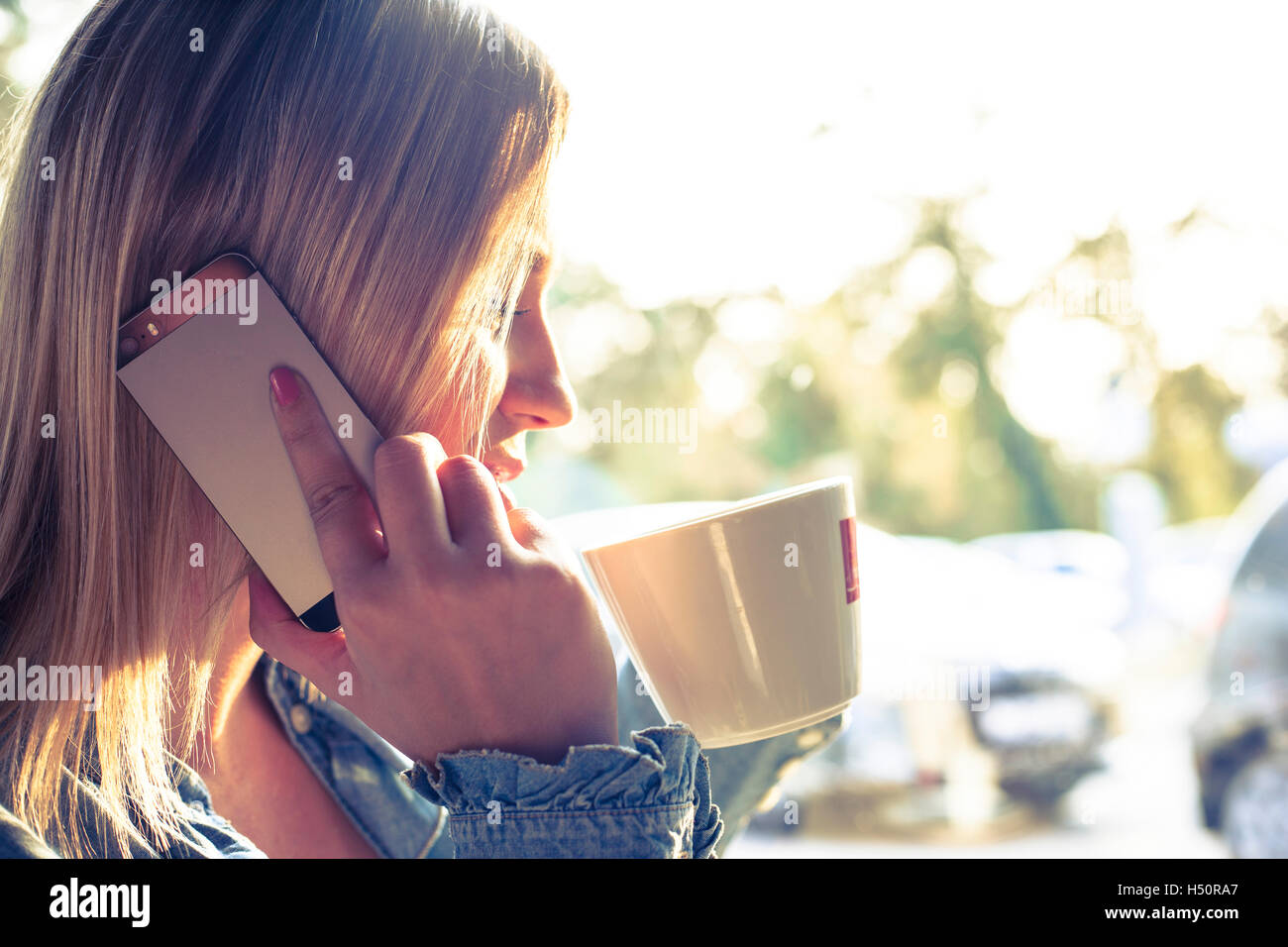 Giovane donna a bere caffè e parlando al telefono cellulare Foto Stock