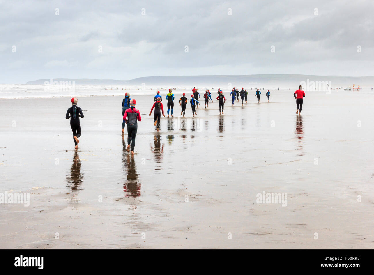 Gli studenti di surf jogging lungo la spiaggia spazzate dal vento a Condino, Devon, Inghilterra, Regno Unito Foto Stock