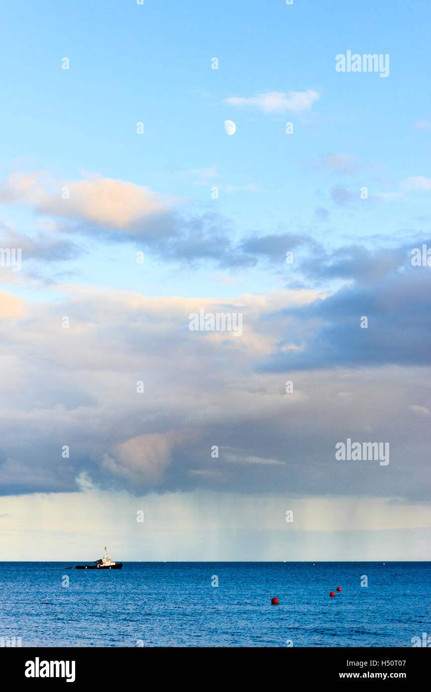 La luna al di sopra di pioggia nuvole sopra il mare a Ringstead Bay, Dorset, England, Regno Unito, un lancio di polizia nella distanza durante il 2012 Olympic eventi marino Foto Stock