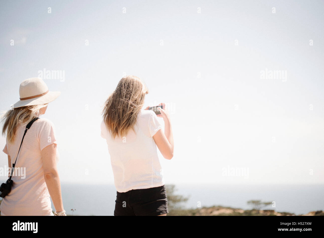 Donna e ragazza adolescente con lunghi capelli biondi all'aperto, tenendo in mano un telefono cellulare per scattare una foto. Foto Stock