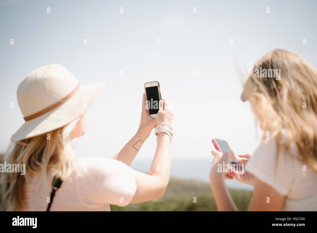 Donna e ragazza adolescente con lunghi capelli biondi all'aperto, tenendo in mano un telefono cellulare per scattare una foto. Foto Stock