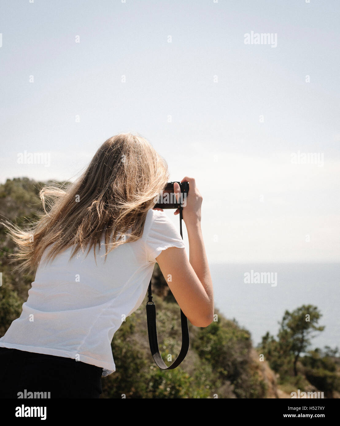 Ragazza con lunghi capelli biondi di guardare attraverso la fotocamera per scattare una foto. Foto Stock