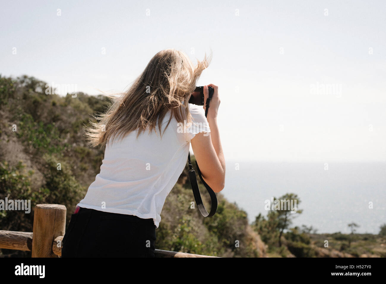 Ragazza con lunghi capelli biondi di guardare attraverso la fotocamera per scattare una foto. Foto Stock