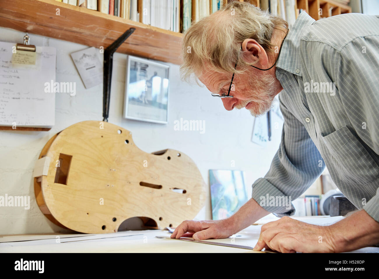 Un liutaio presso il suo tavolo da disegno disegno fuori i piani e la bozza di un nuovo strumento. Foto Stock