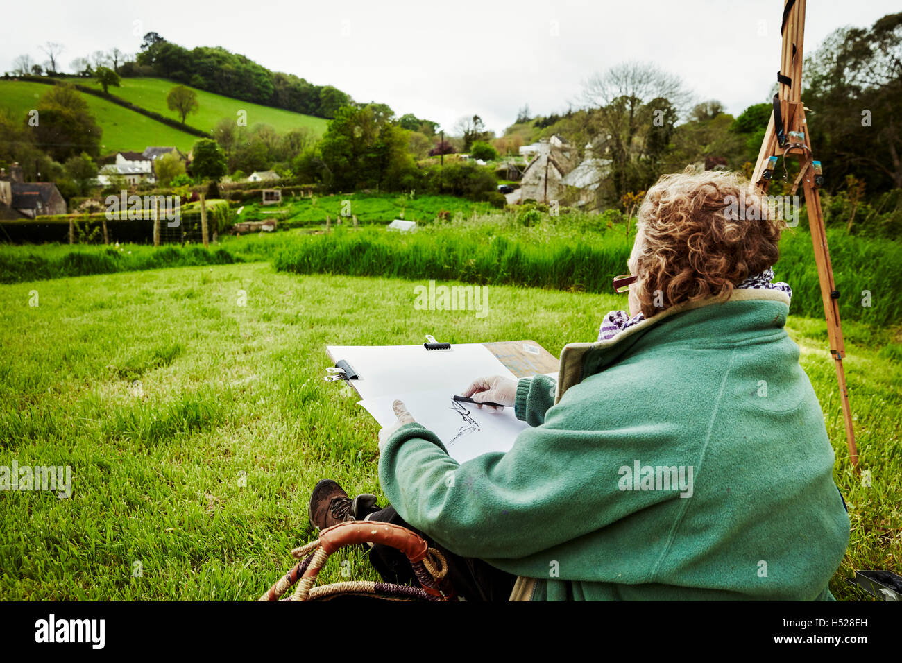 Una donna artista delineando con carboncino su carta, seduto a terra all'esterno. Foto Stock