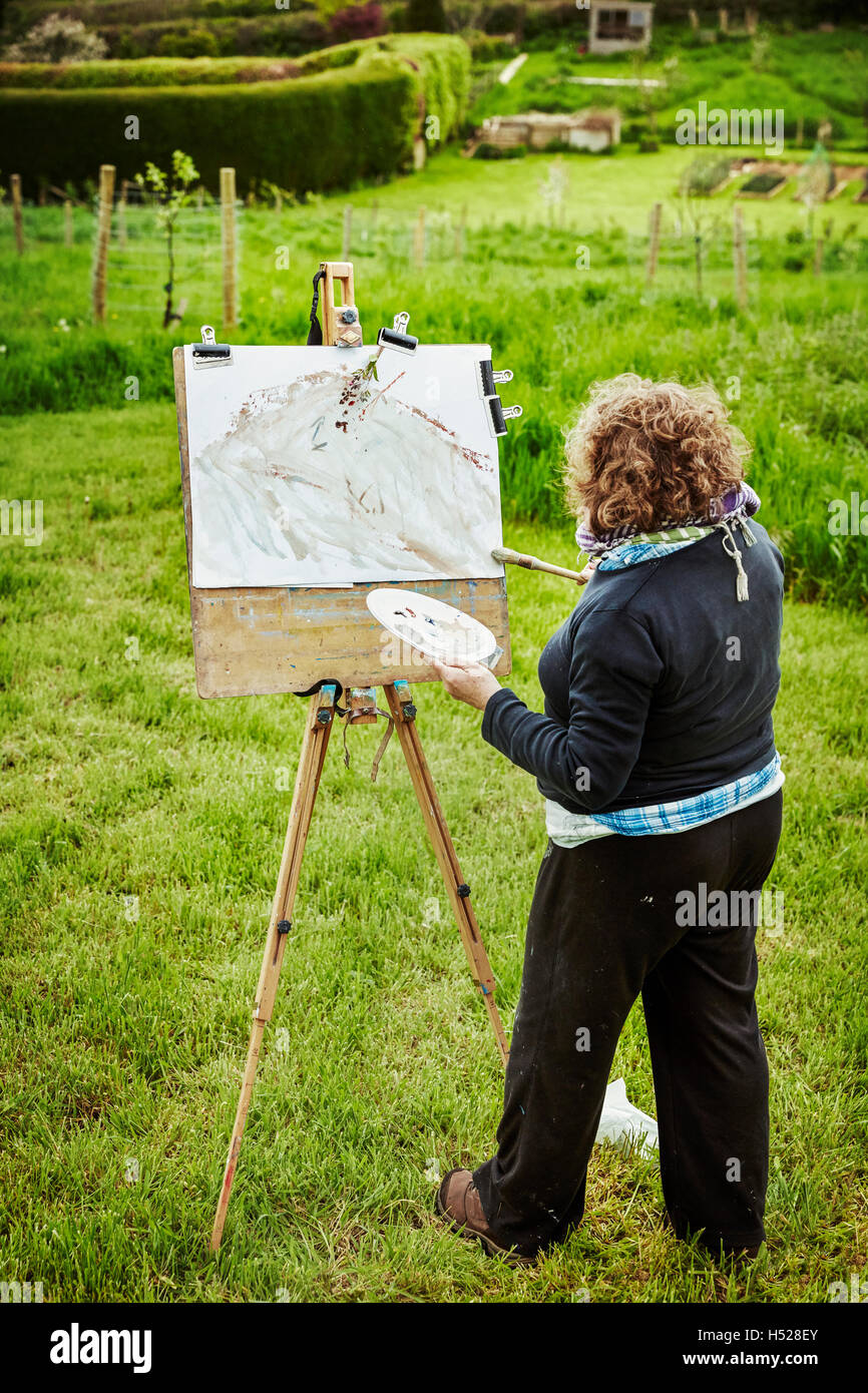 Una donna artista in esterni al cavalletto, applicazione di vernice sulla carta con un pennello. Foto Stock