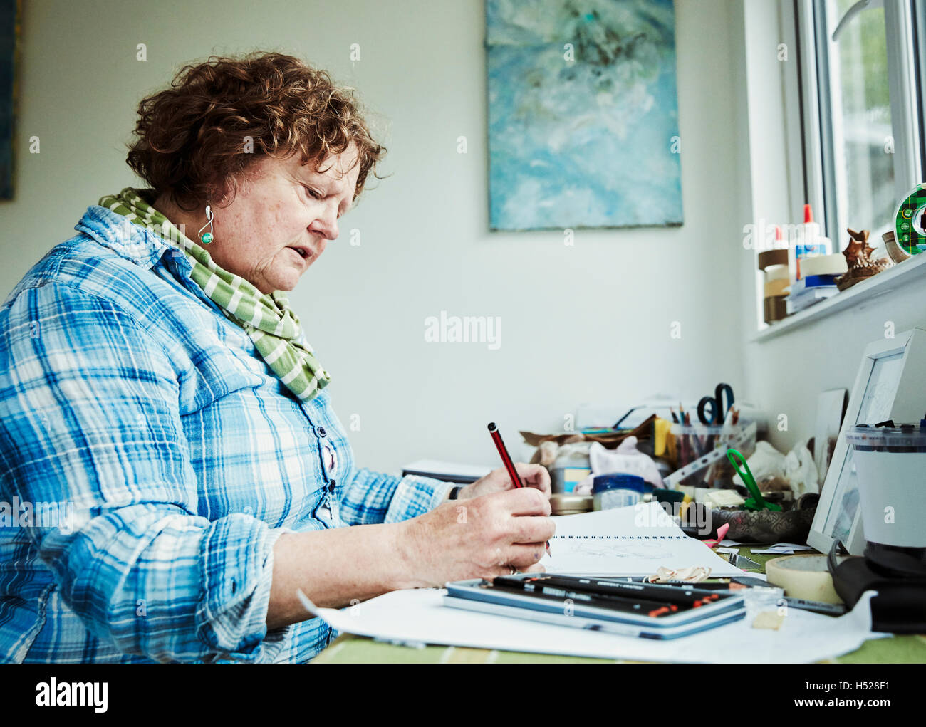 Una donna artista che lavora a una tabella tenendo un disegno a matita su carta. Foto Stock