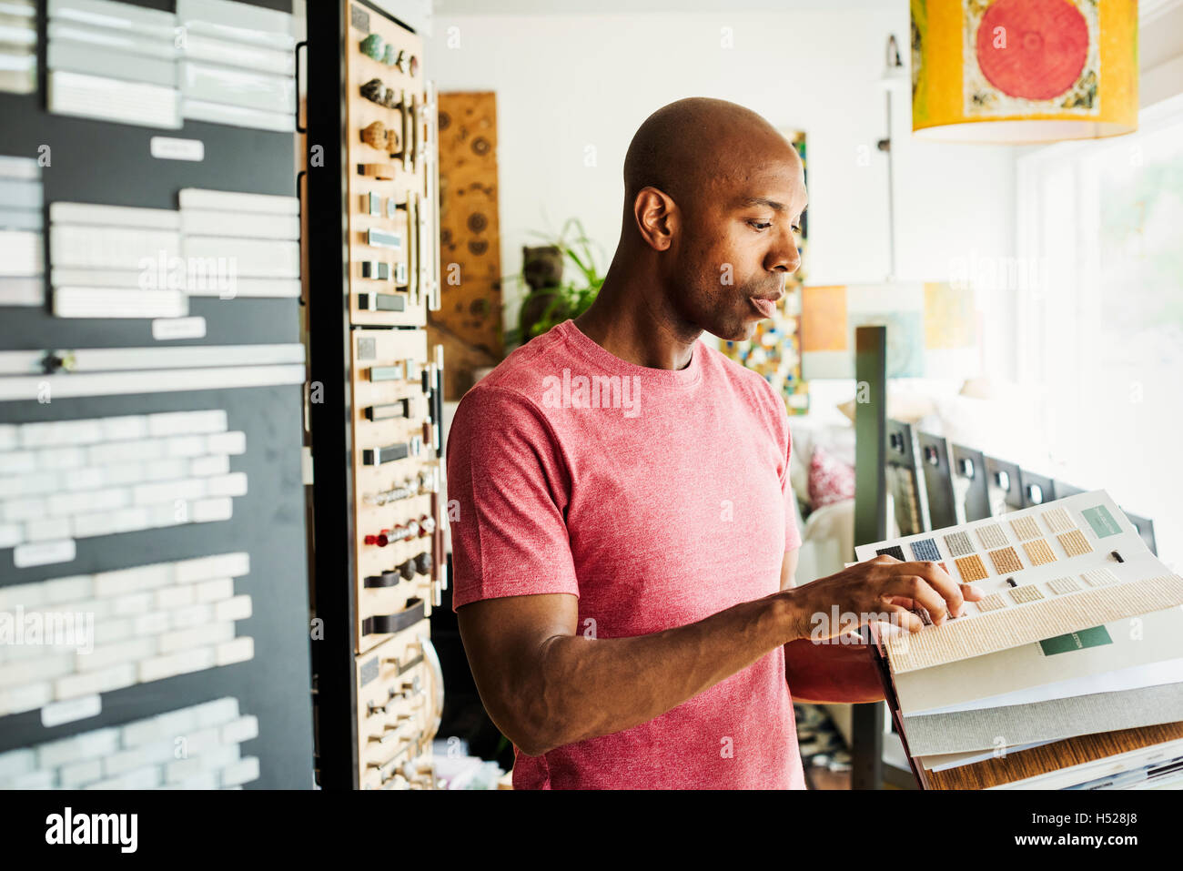 Uomo che guarda un campione prenota in interior design store. Campioni di piastrelle sulle pareti. Foto Stock