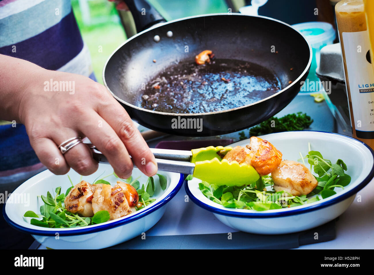 Donna in corrispondenza di un fornello da campeggio, preparare due piastre con capesante fritte e erbe aromatiche fresche. Foto Stock
