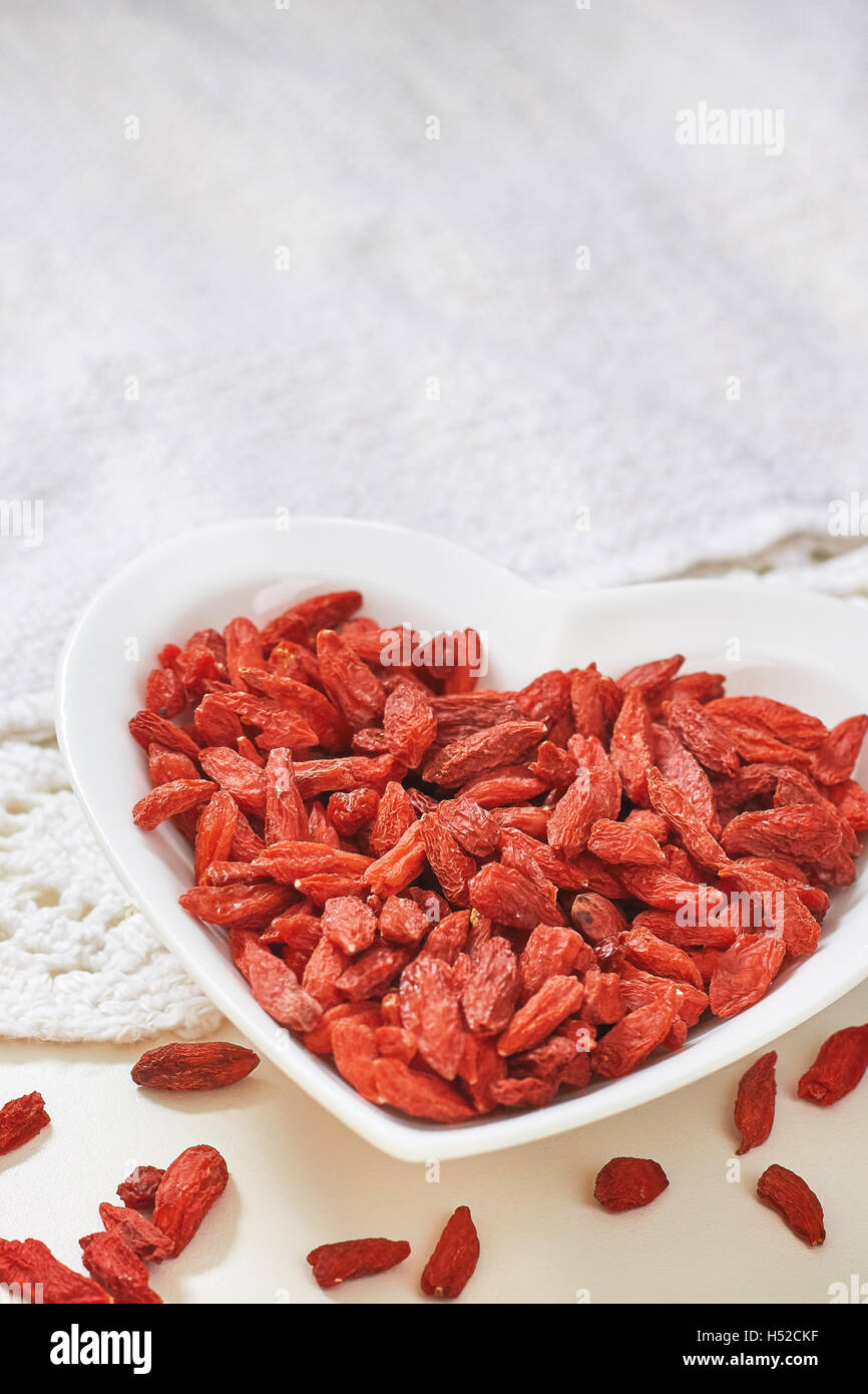 Essiccati goji bacche nel cuore di ceramica a forma di ciotola sul tavolo bianco. Spazio di copia Foto Stock