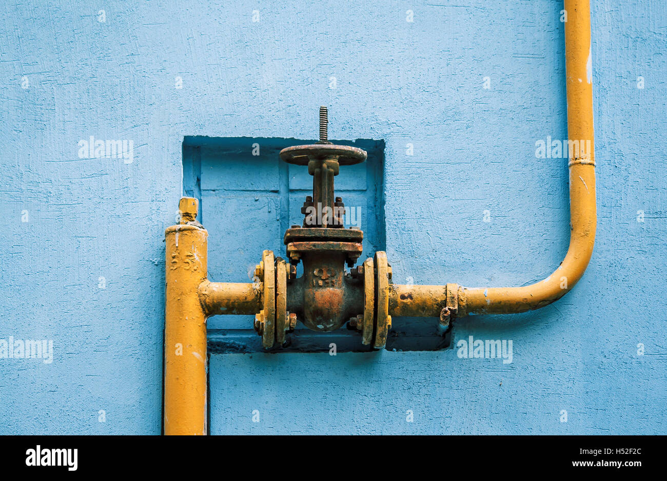 Giallo della tubazione di gas con una valvola sull'azzurro del muro di un edificio Foto Stock