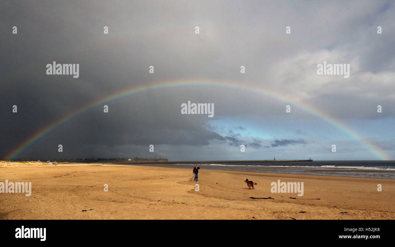 Un arcobaleno si sviluppa su Knotts Appartamenti in Tynemouth come un uomo cammina il suo cane su South Shields beach. Foto Stock