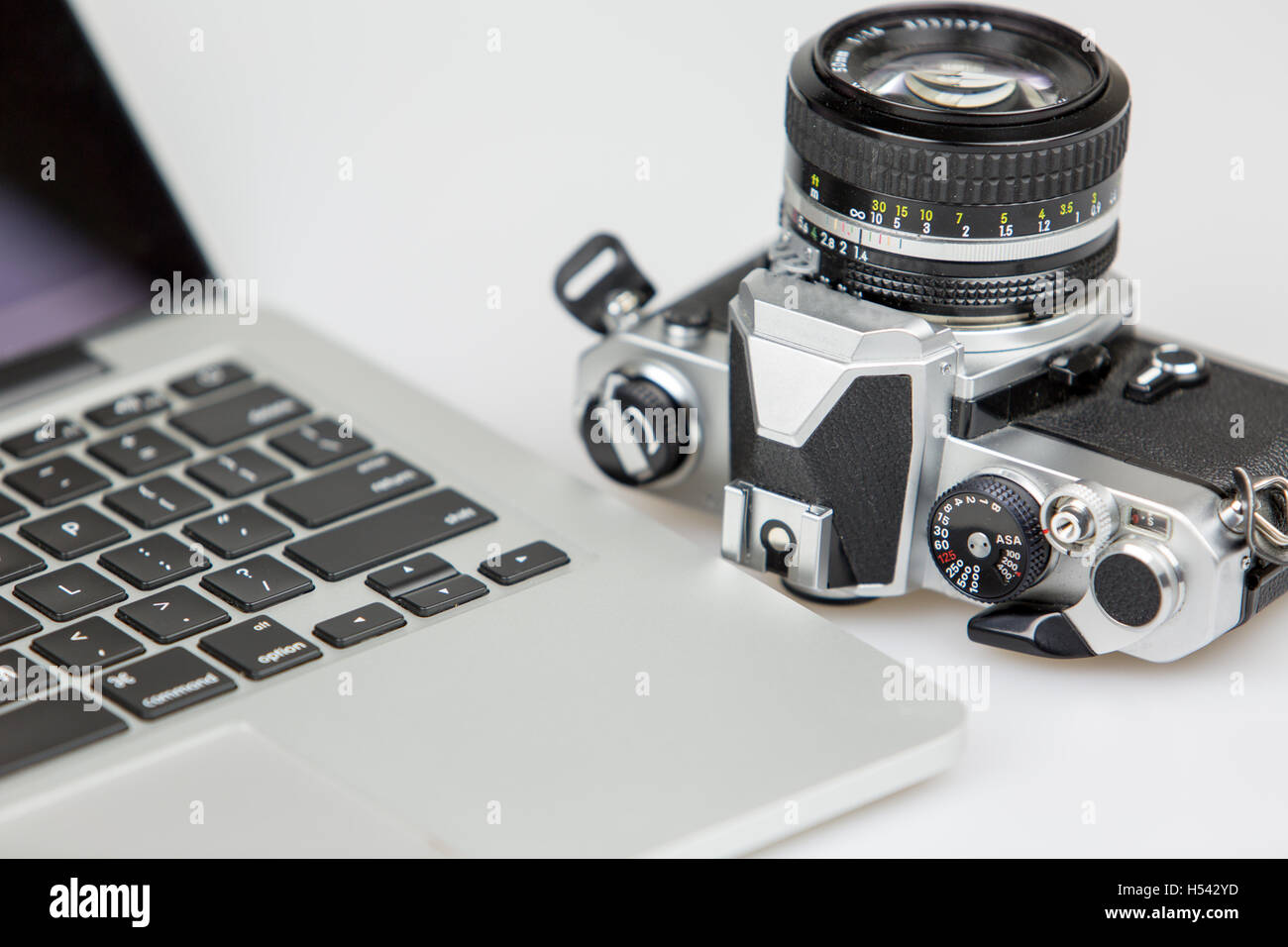 Fotocamera vintage e un computer portatile su un tavolo bianco con sfondo bianco. Foto Stock