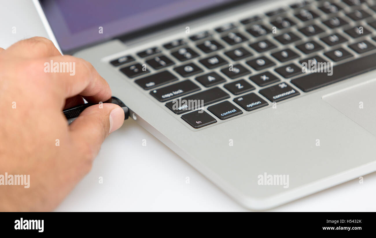 Una persona di sesso maschile di tamponamento dati USB stick viaggiatore in un notebook. closeup shot dal lato sinistro Foto Stock