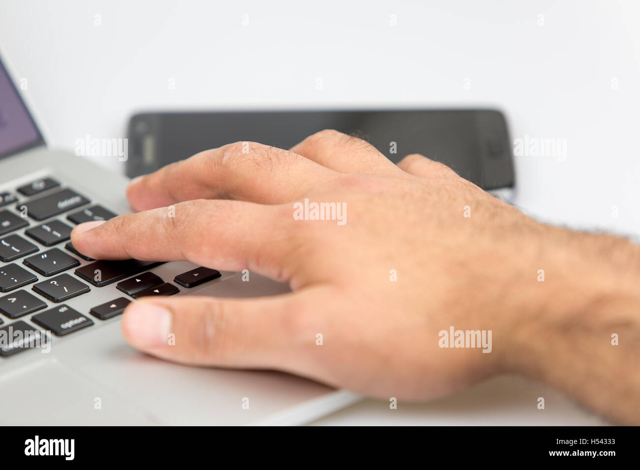 Uomo al lavoro su un notebook con lo smartphone giacente su un tavolo in background. sia spento. studio shot su uno sfondo bianco. Foto Stock