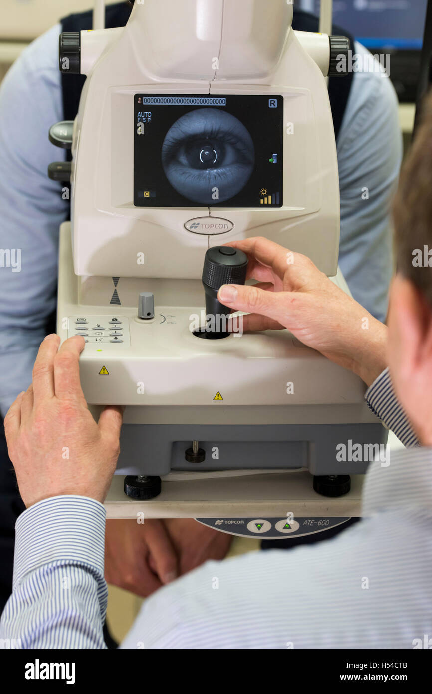 Un ottico effettuando un occhio test utilizzando una tomografia di coerenza ottica (PTOM) macchina. Foto Stock