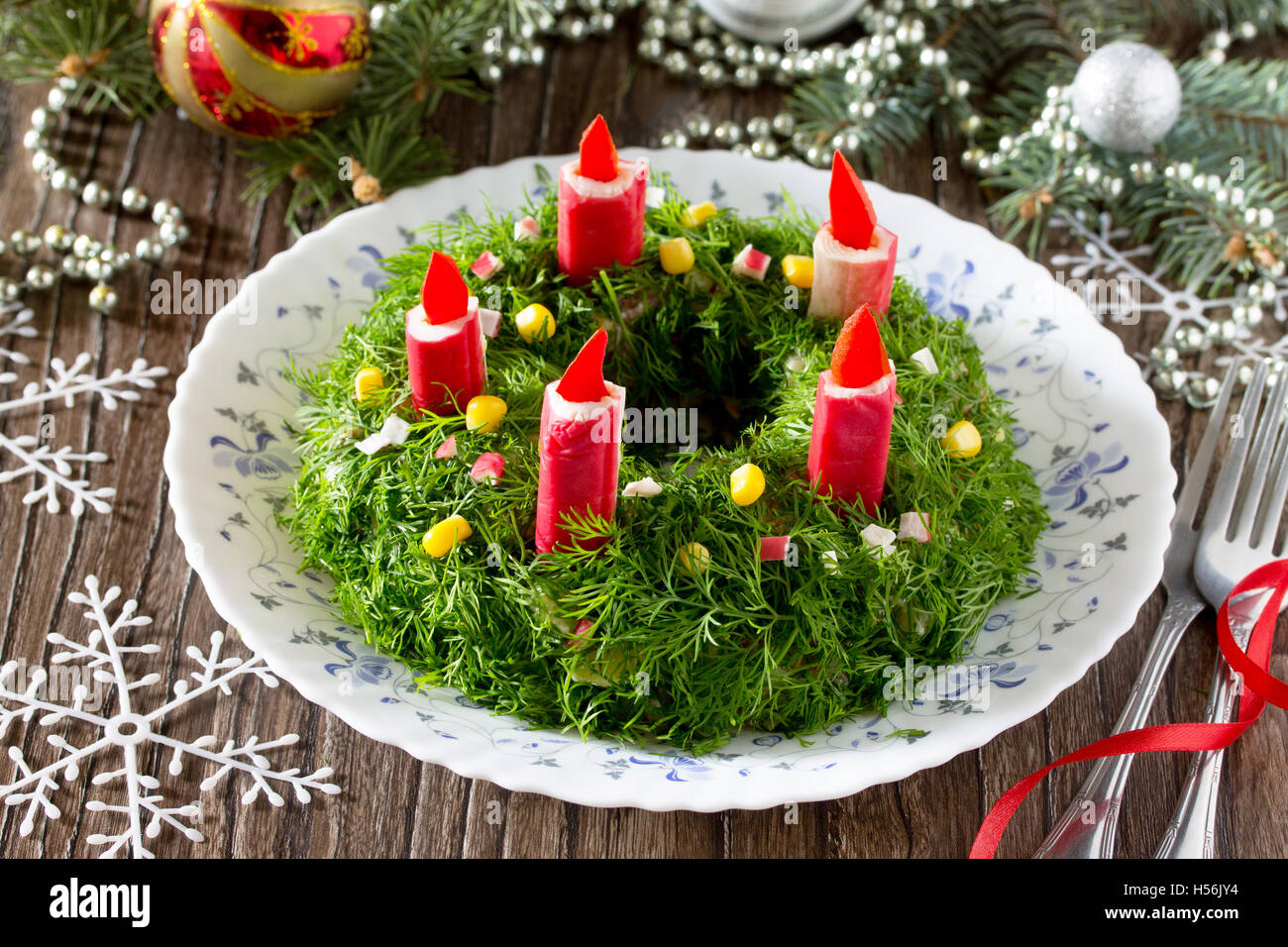 Natale con insalata di riso, mais, cetriolo e bastoncini di granchio. Decorate corona di Avvento e candele. Foto Stock