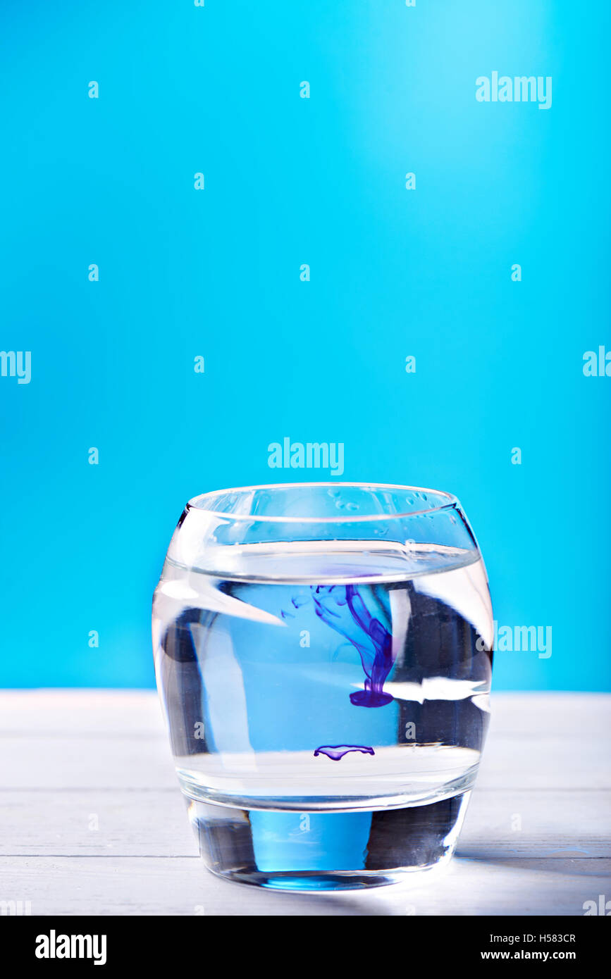 Una goccia di liquido di colore viola è stato appena versata in un chiaro wineglass a sfondo blu Foto Stock