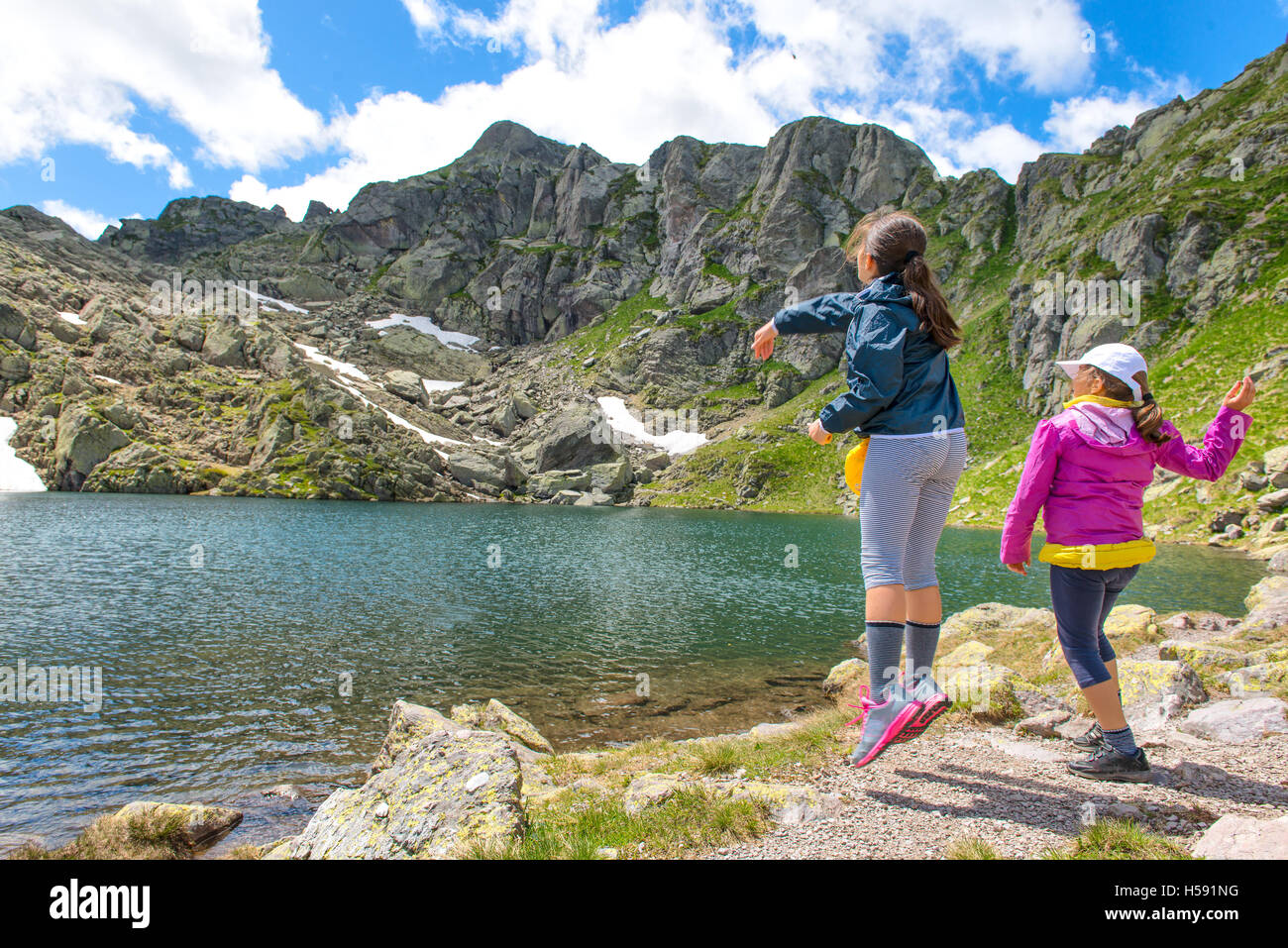 Due ragazze gettare pietre in un lago di montagna Foto Stock