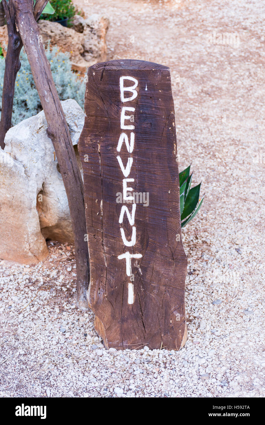 Simbolo di benvenuto in italiano. Su un pezzo di legno grezzo, riciclaggio oggetti usati, ingresso un giardino. Foto Stock