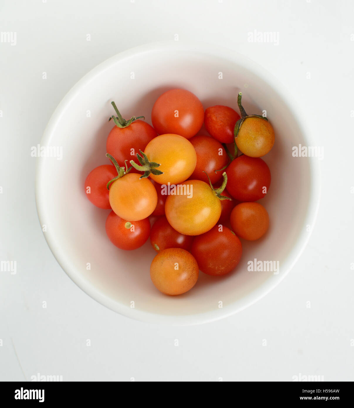 Ultimo pomodori ciliegia della stagione nella piccola rotonda ciotola bianco su sfondo bianco. Semplice vita ancora in formato quadrato. Foto Stock