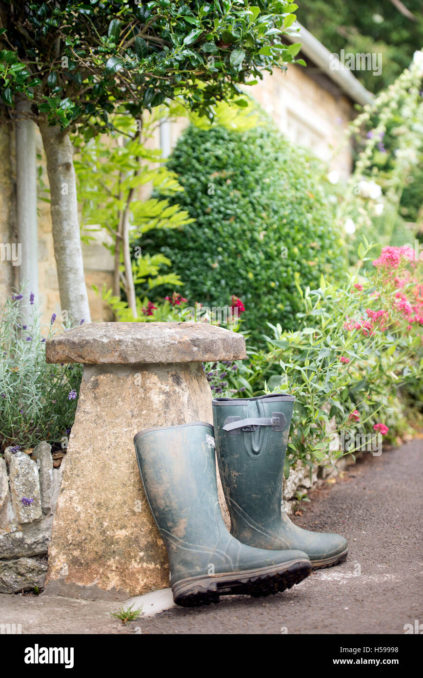 Un paio di stivali da pioggia appoggiata contro una pietra staddle al di fuori di un paese Cotswold cottage, REGNO UNITO Foto Stock