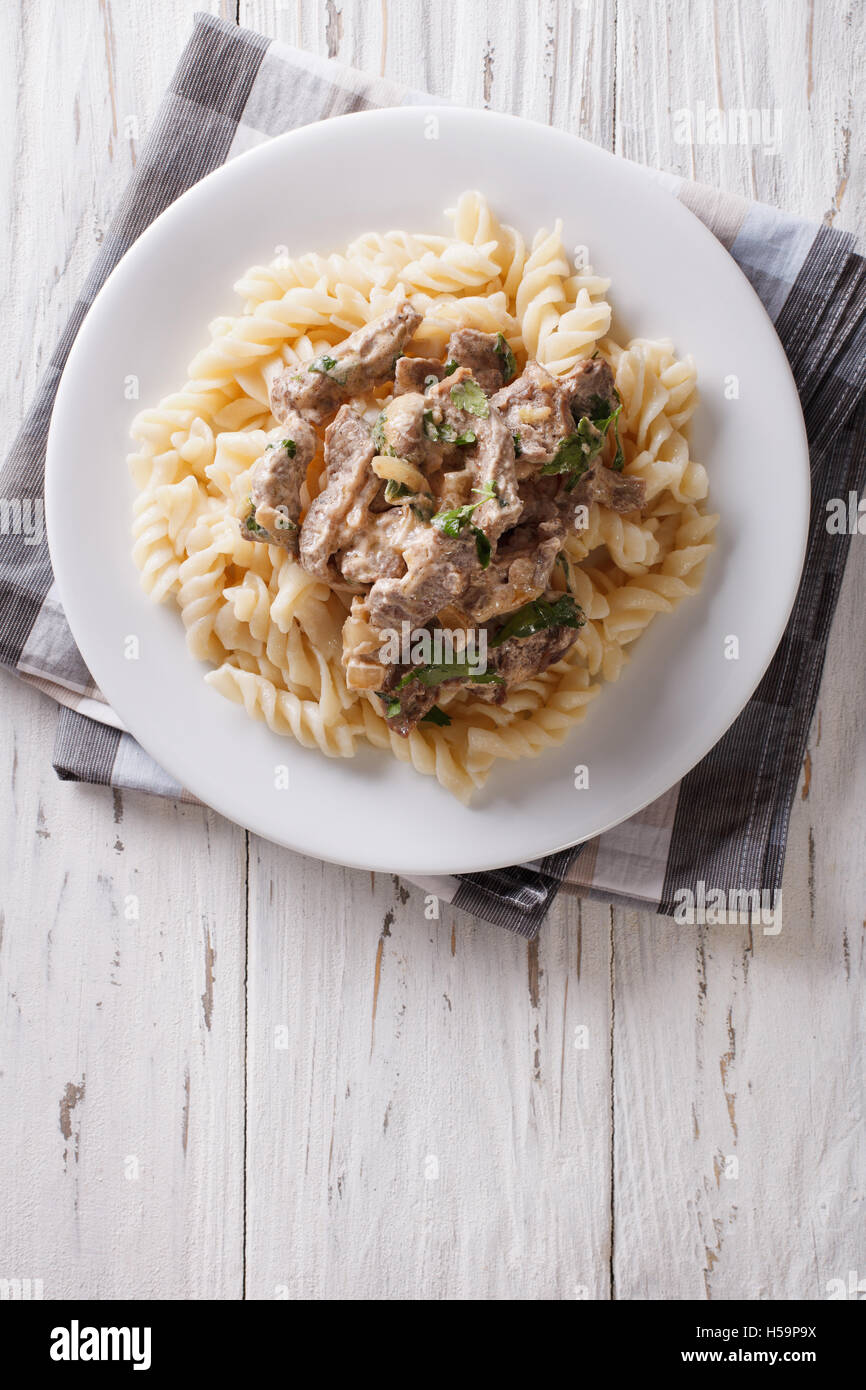 Deliziosa carne di manzo stroganoff con pasta fusilli su una piastra sul tavolo. Vista verticale da sopra Foto Stock