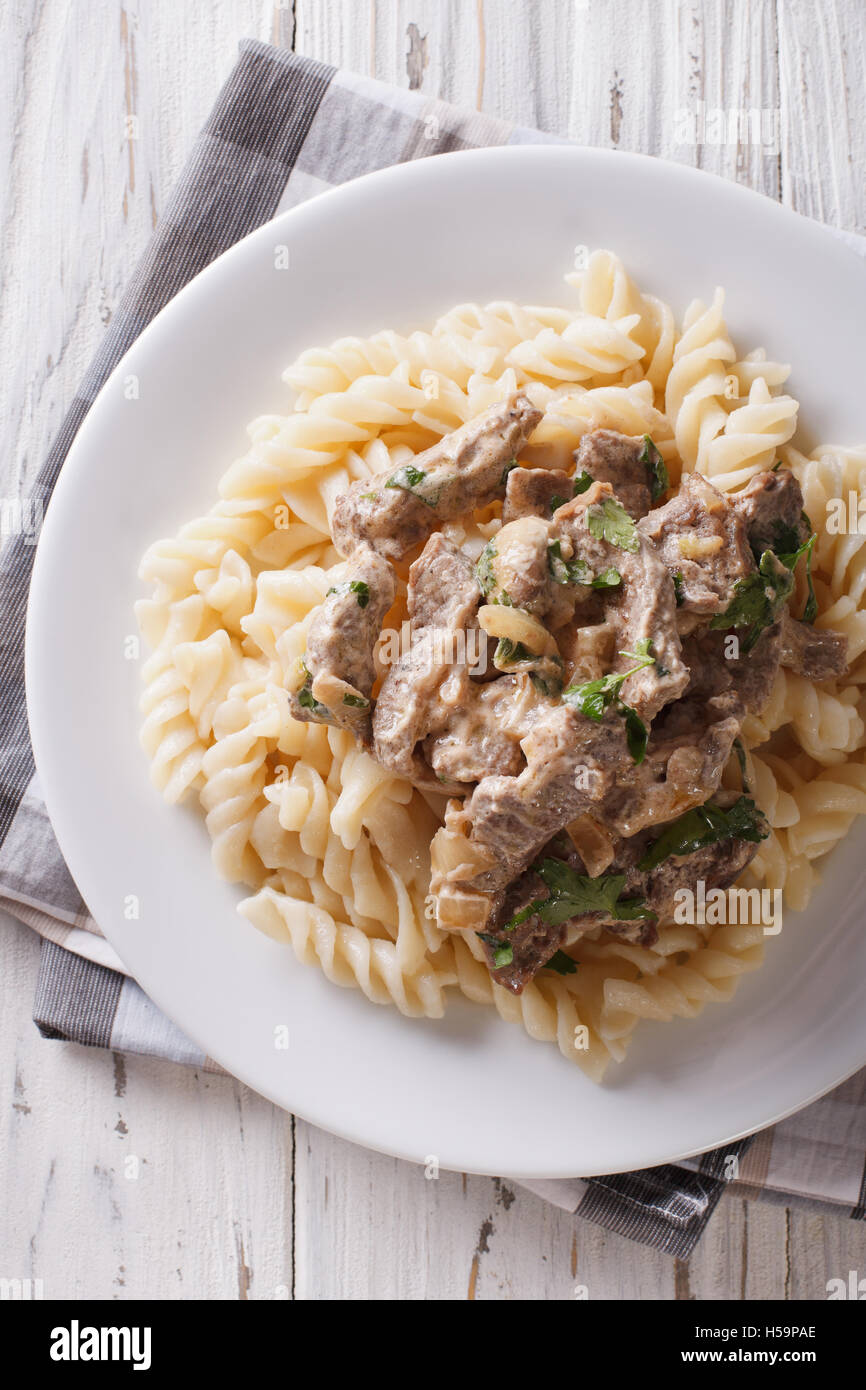 Carni bovine stroganoff e pasta fusilli close-up su una piastra sul tavolo. Vista verticale da sopra Foto Stock