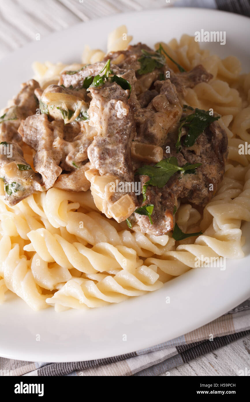 Carni bovine stroganoff con pasta fusilli closeup su una piastra sul piano verticale. Foto Stock