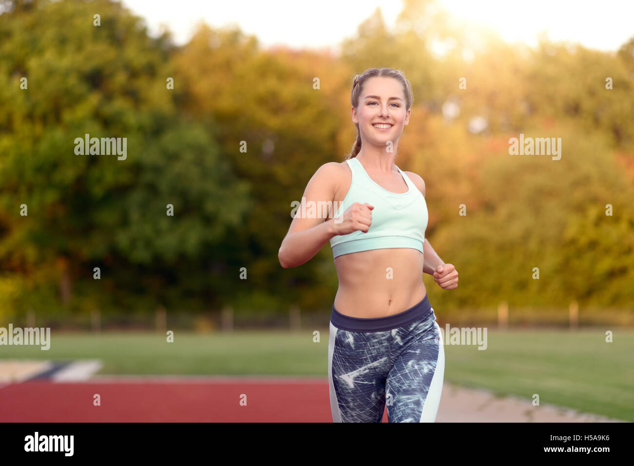Carino giovane femmina runner nel serbatoio superiore con race track e alberi in background per il concetto di idoneità Foto Stock