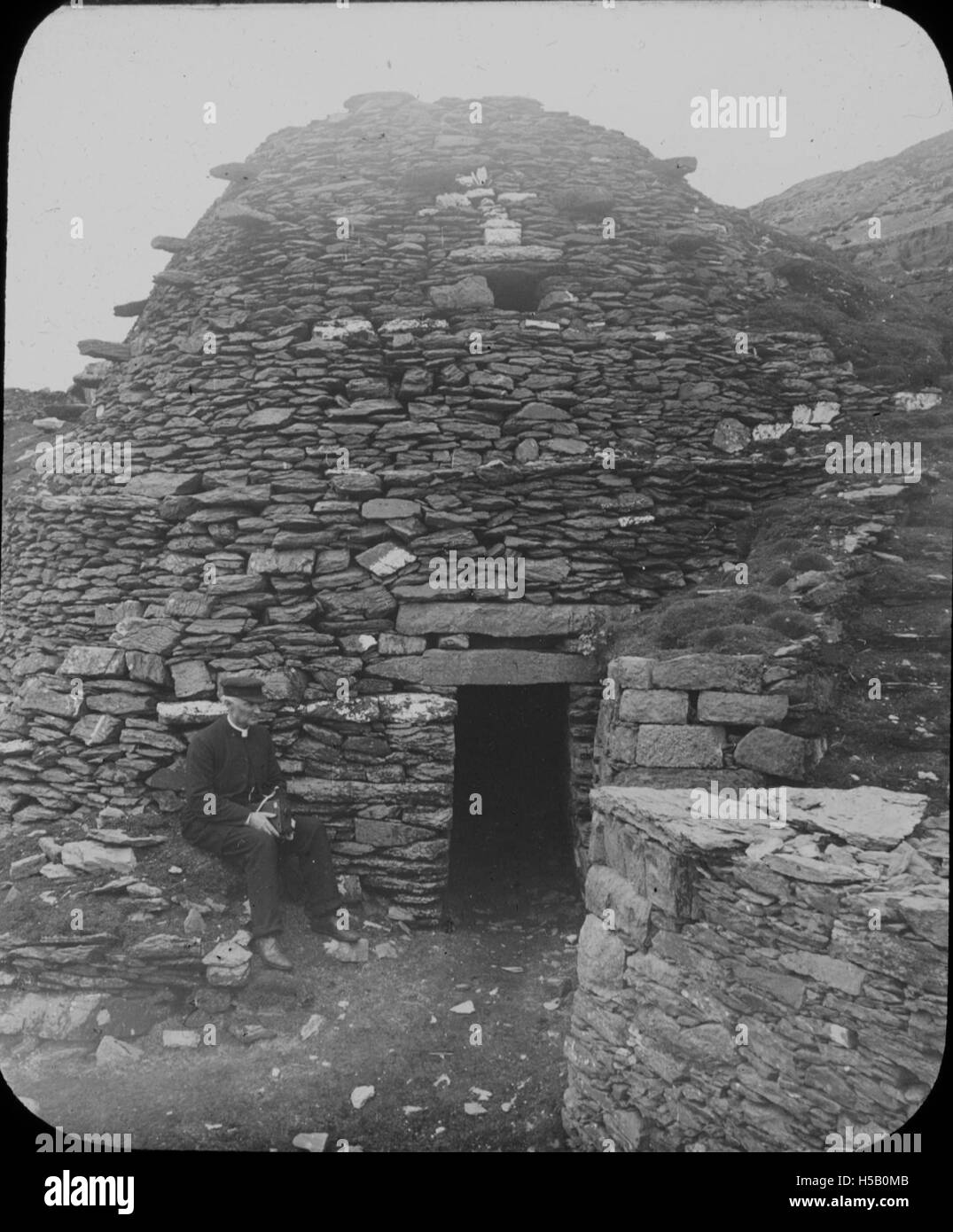 Un prete siede all'ingresso di una cella a Skellig Michael, un'isola isolata al largo della costa della contea di Kerry, in Irlanda. Il sito è noto per la sua storia monastica, con capanne ben conservate dell'alveare. Foto Stock