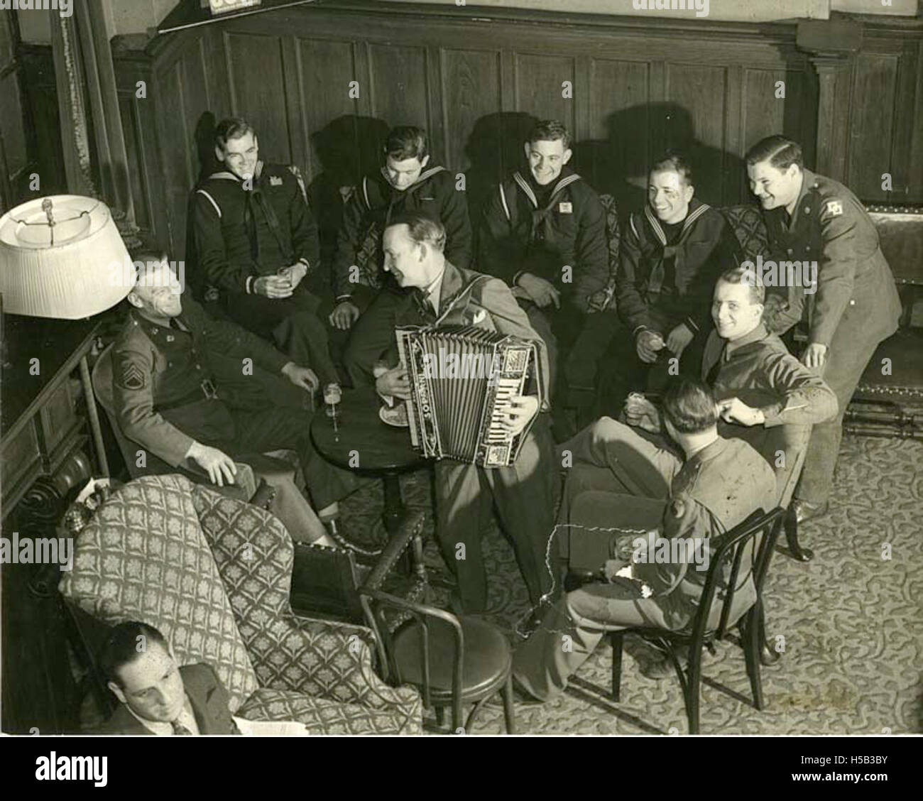 Fotografia dei membri del City Athletic Club di New York, ascoltando attentamente un fisarmonicista durante un incontro, evidenziando gli eventi sociali e gli impegni culturali del club. Foto Stock