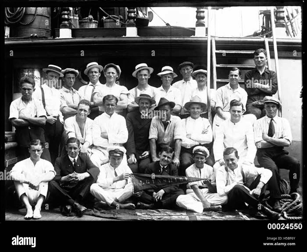 Questo ritratto di gruppo presenta ventiquattro uomini e ragazzi a bordo del ponte dell'ELGINSHIRE, una nave probabilmente associata ad attività marittime. La foto cattura individui, alcuni in abbigliamento navale, durante un periodo storico, che riflettono le persone coinvolte in viaggi o commerci marittimi. Foto Stock